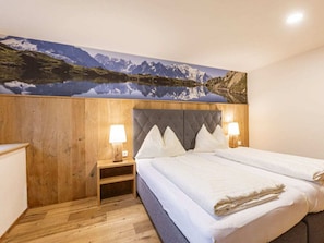 A hotel room with a bed, two bedside lamps, a wooden headboard, and a large wall mural of a mountain landscape. - Apartment With 1 Bedroom (Sankt Georgen am Kreischberg)