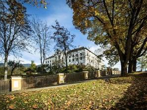 A large, historic building with a symmetrical facade, surrounded by a well-maintained lawn and a wooden fence.