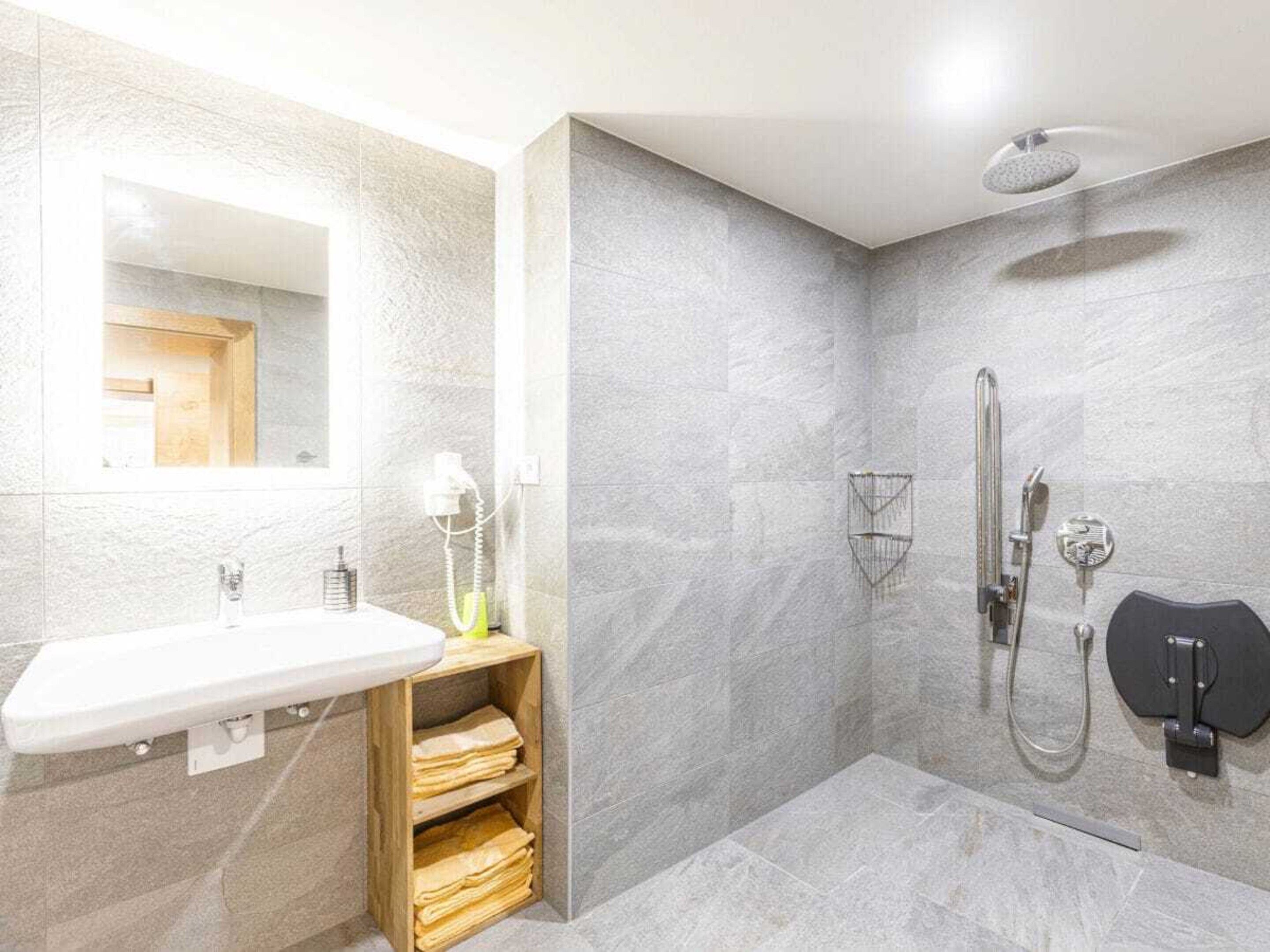 Un bagno moderno con un lavandino bianco, uno specchio, una doccia con soffione manuale e un portasciugamani.