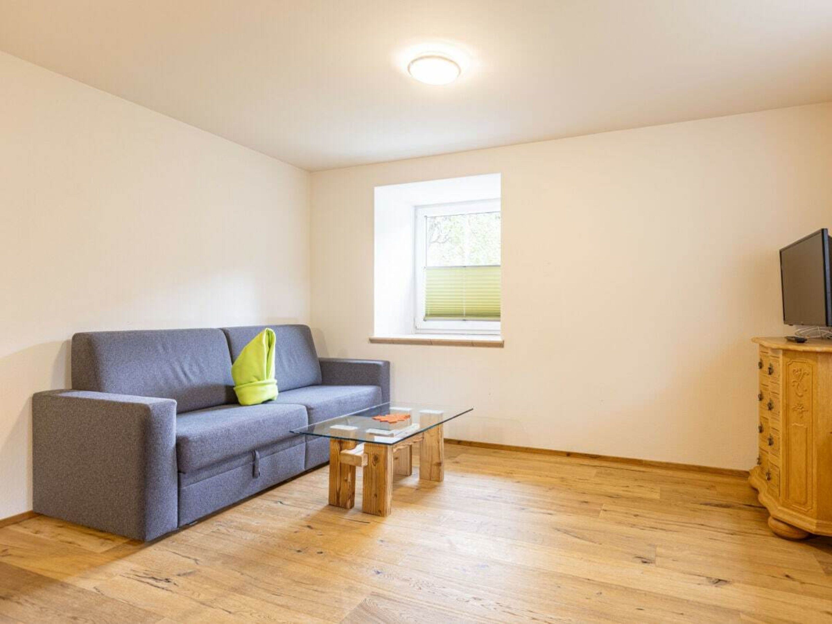 A living room with a grey sofa, a glass coffee table, a wooden cabinet, and a television on top.