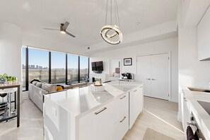 Una cocina moderna con una isla central, un área de comedor con sofá y un amplio ventanal con vista a la ciudad.