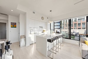 Una cocina moderna con muebles blancos, una isla central con taburetes y un ventanal con vistas a la ciudad.
