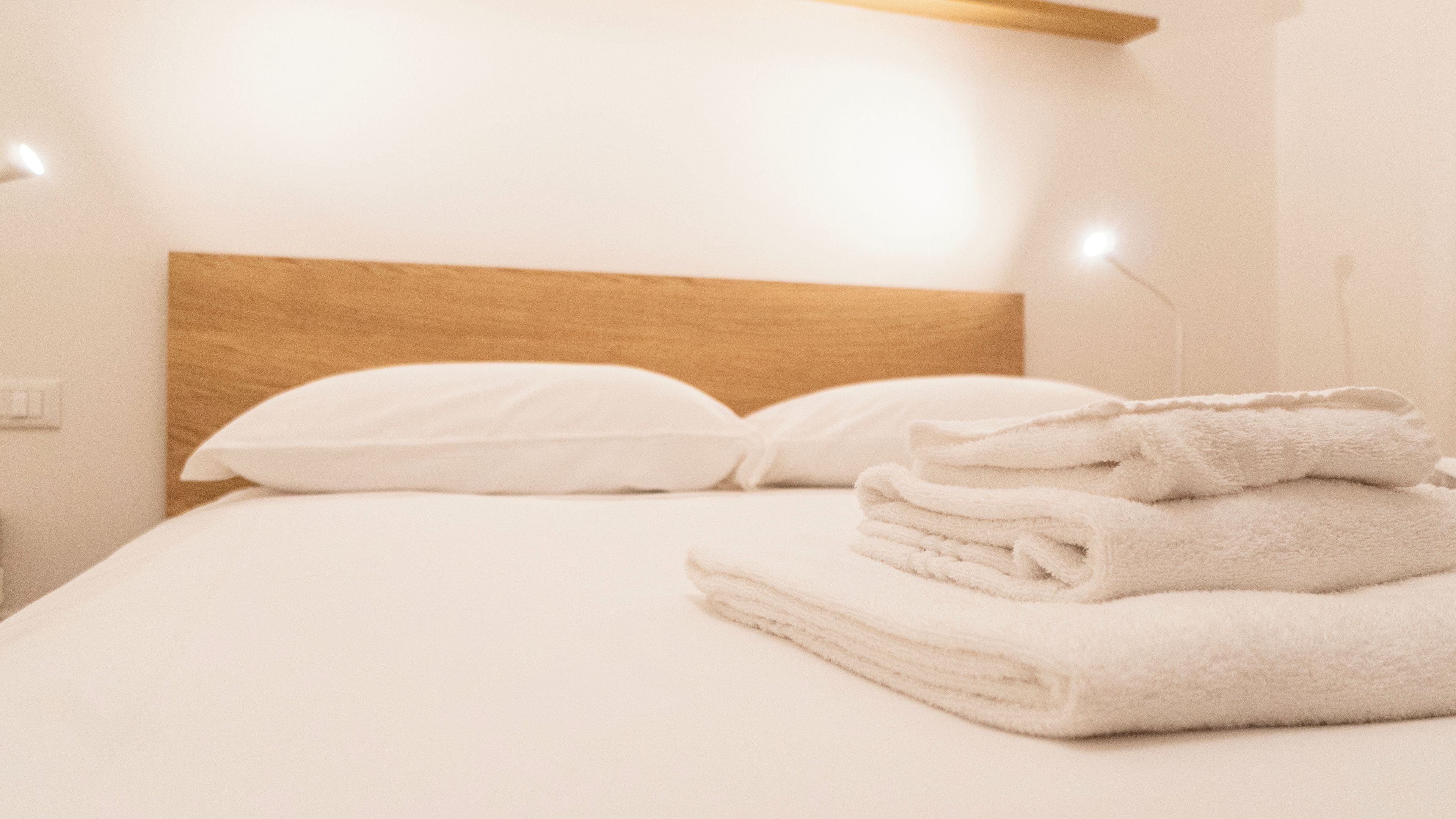 A neatly made bed with white linens and a stack of folded towels.