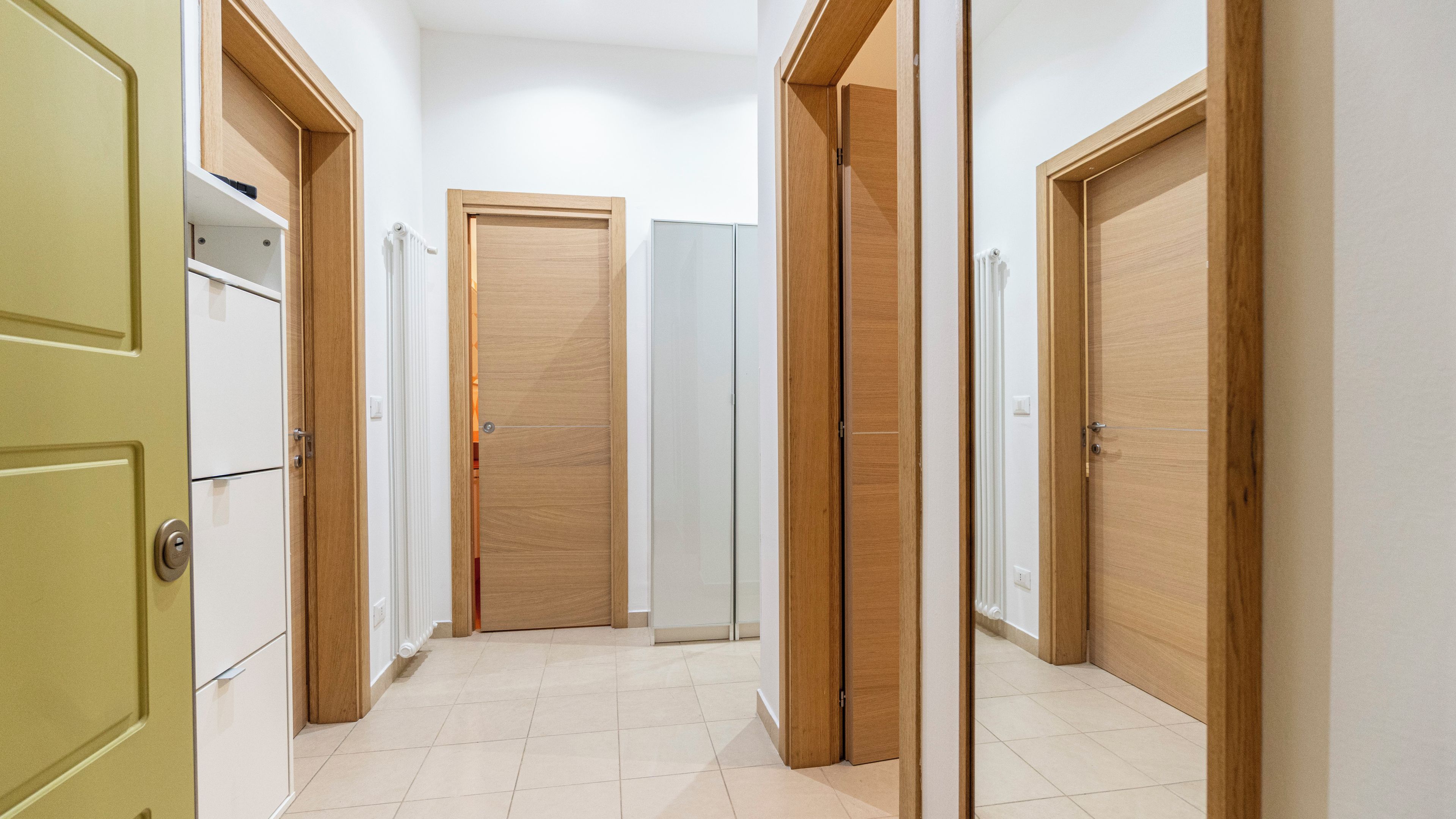 Un pasillo con puertas de madera, un radiador y suelo de baldosas.