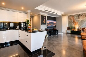Eine moderne Küche mit einer zentralen Kochinsel, ein Essbereich mit Fernseher und ein Wohnzimmer mit Sofa und Wanddeko.