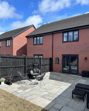 A residential building with a brick exterior, a patio area with outdoor furniture, and a wooden fence. - Modern, stylish house in Anfield (an Áit Bheag) (Liverpool)