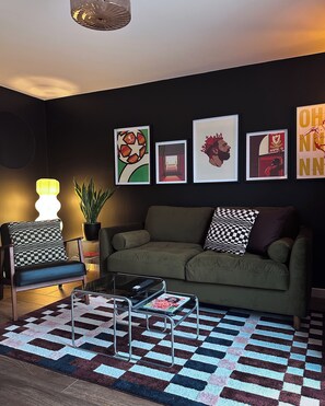 A living room with a green sofa, checkered cushions, a glass coffee table, and a patterned rug. - Modern, stylish house in Anfield (an Áit Bheag) (Liverpool)