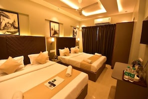 A hotel room with two beds, a desk with a chair, a ceiling fan, and artwork on the walls. - Hotel Aura Nr Kokilaben Hospital (Mumbai)