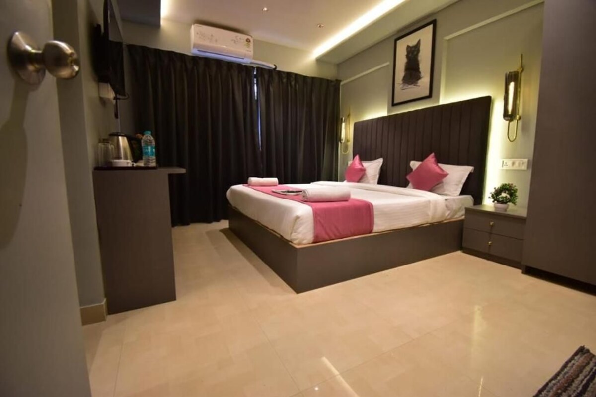 A modern hotel room with a large bed, bedside tables, a desk, and a wall-mounted air conditioner.