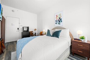 Ein Hotelzimmer mit Bett, Nachttisch, Schreibtisch, Stuhl und einem an der Wand montierten Fernseher.