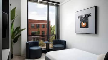 Une chambre d’hôtel moderne avec une grande fenêtre, deux fauteuils, un lit et un tableau encadré au mur.