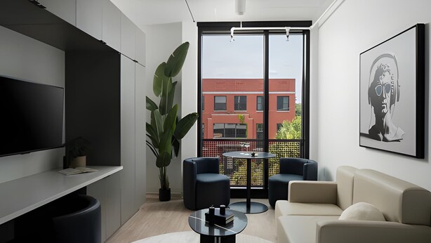 A modern living room with a flat-screen TV, a sofa, a coffee table, and a large window with a view of a red building. - Miles at Ybor - Tampa (Tampa)