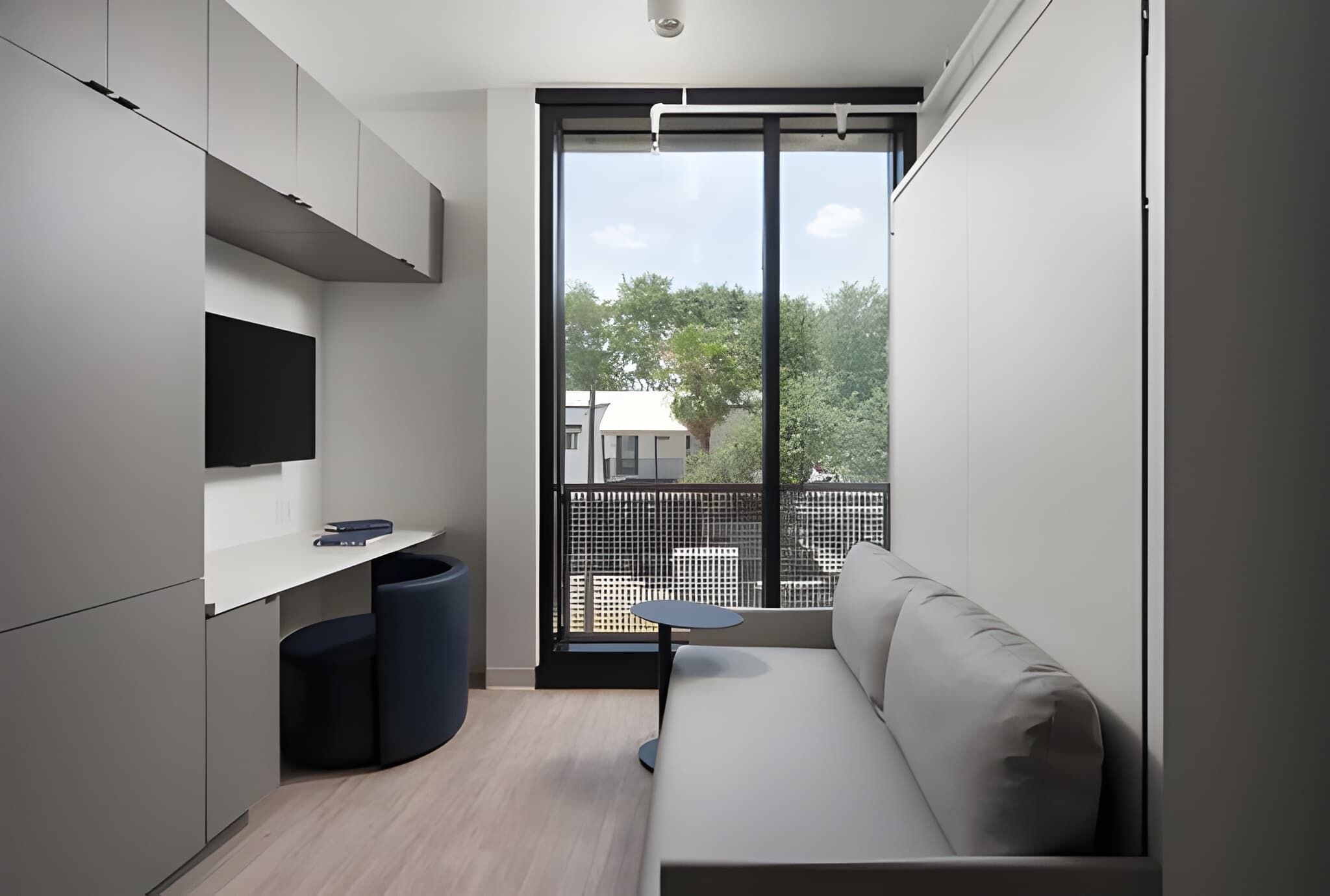 Ein moderner, kompakter Wohnraum mit einer Couch, einem kleinen Tisch und einem an der Wand befestigten Fernseher.