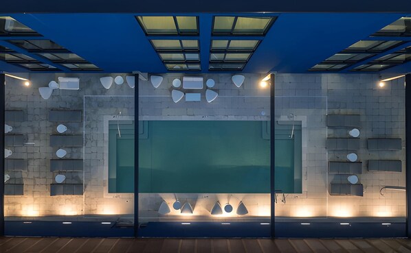 Un interior moderno con un amplio panel de vidrio central, estanterías geométricas y un techo azul con tragaluces.