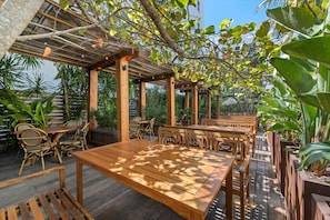 An outdoor patio area with wooden tables and chairs, surrounded by lush greenery and a pergola structure. - Conventions Ctr & Collins Ave is nearby, Junior King Studio (Miami Beach)