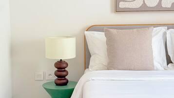 Un dormitorio con cama, almohadas, una mesita de noche con lámpara y una obra de arte en la pared.