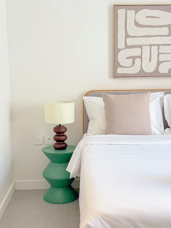 A bedroom with a bed, pillows, a bedside table with a lamp, and a wall art piece.
