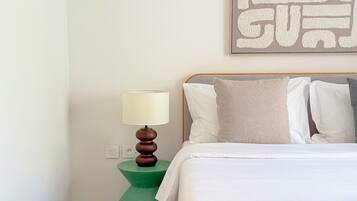 A neatly made bed with white linens, a green nightstand with a lamp, and a wall-mounted artwork.