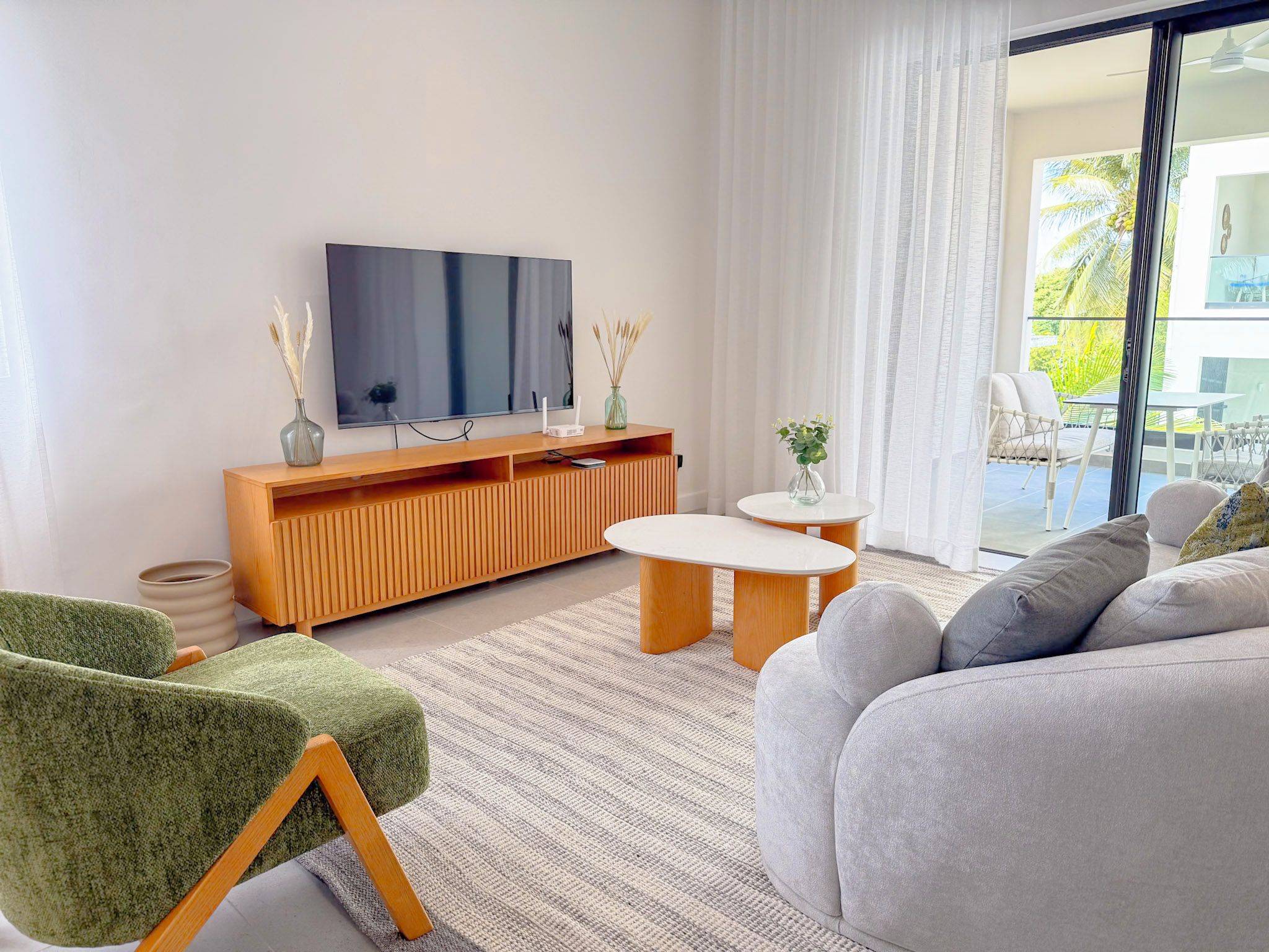 A modern living room with a flat-screen TV, wooden console, green armchair, grey sofa, and a small round table.