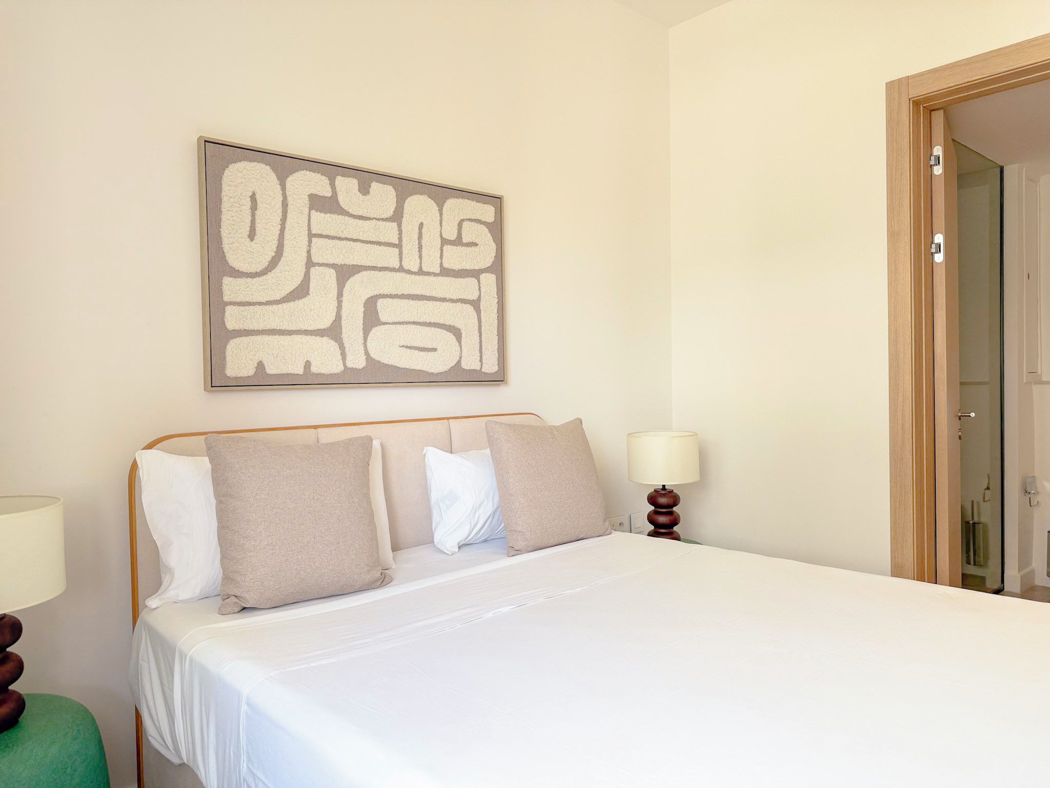 A neatly made bed with a headboard, a bedside lamp, and a wall-mounted abstract art piece.