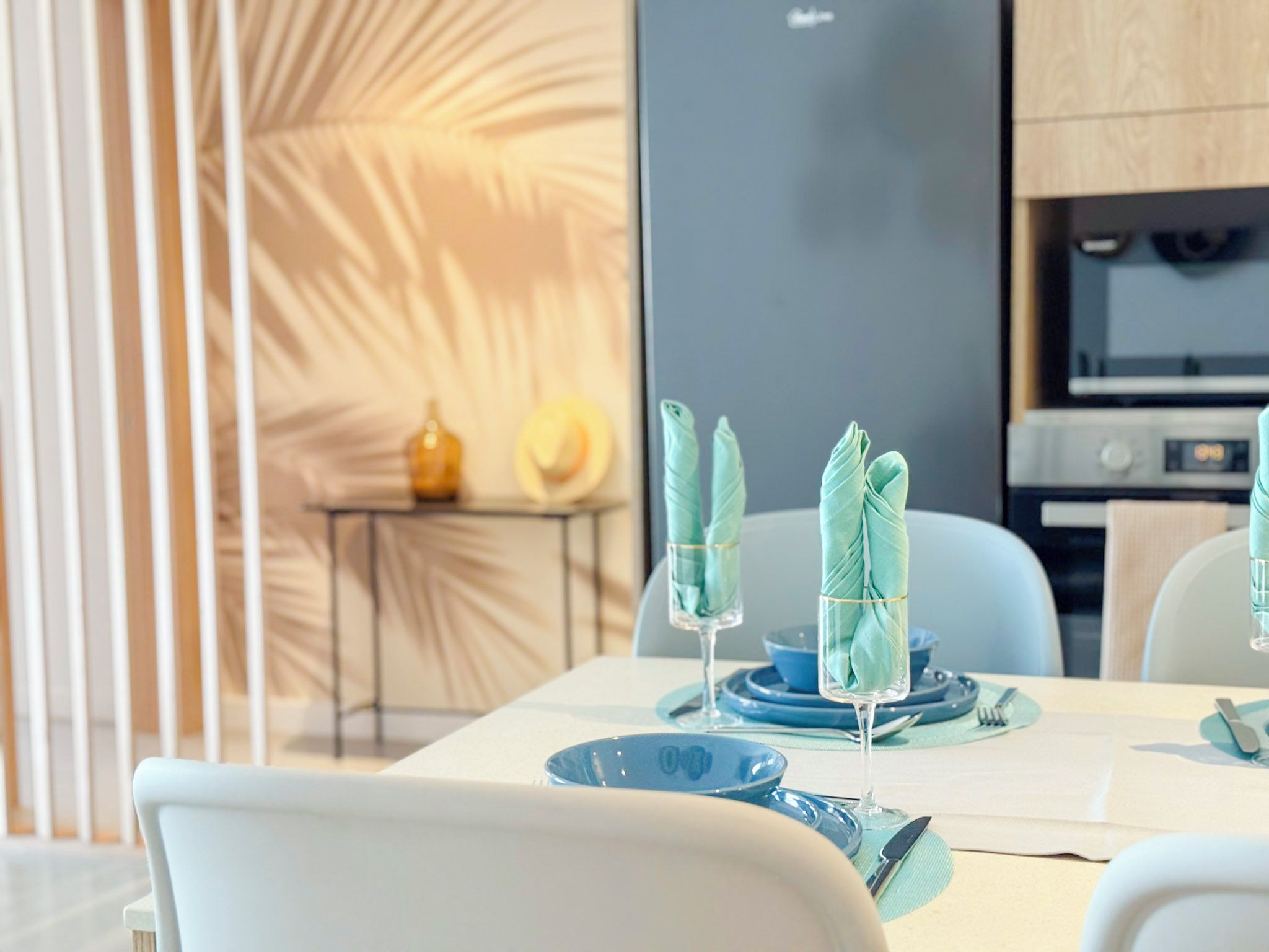 A modern dining area with a table set for two, featuring blue plates and glassware.