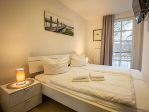 A hotel room with a bed, nightstands, a lamp, a painting, a window with curtains, and a radiator. - Apartment in Balm With Swimming Pool (Benz)