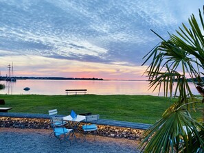A tranquil lakeside setting with a bench and a table with chairs, surrounded by a grassy area and a stone wall. - Apartment in Balm With Swimming Pool (Benz)