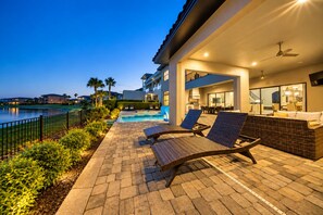 A poolside area with lounge chairs, a pool, and a building with a balcony. - Enchanted Lakeview Mansion | 8BR Reunion Resort Home with Pool, Spa, Theater & Themed Rooms (Kissimmee)