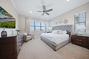 A bedroom with a large bed, a ceiling fan, a dresser, a nightstand, and a view of the outdoors. - Enchanted Lakeview Mansion | 8BR Reunion Resort Home with Pool, Spa, Theater & Themed Rooms (Kissimmee)