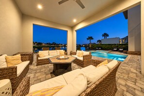 An outdoor patio with wicker furniture, a fire pit, and a swimming pool. - Enchanted Lakeview Mansion | 8BR Reunion Resort Home with Pool, Spa, Theater & Themed Rooms (Kissimmee)