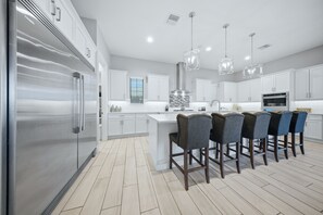 A modern kitchen with a large island, stainless steel appliances, and bar stools. - Enchanted Lakeview Mansion | 8BR Reunion Resort Home with Pool, Spa, Theater & Themed Rooms (Kissimmee)