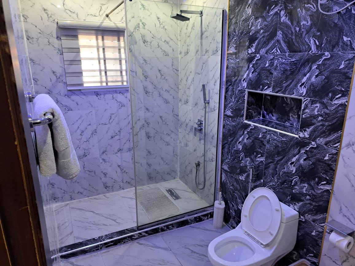 A bathroom with a glass-enclosed shower, a toilet, and marble-patterned walls.