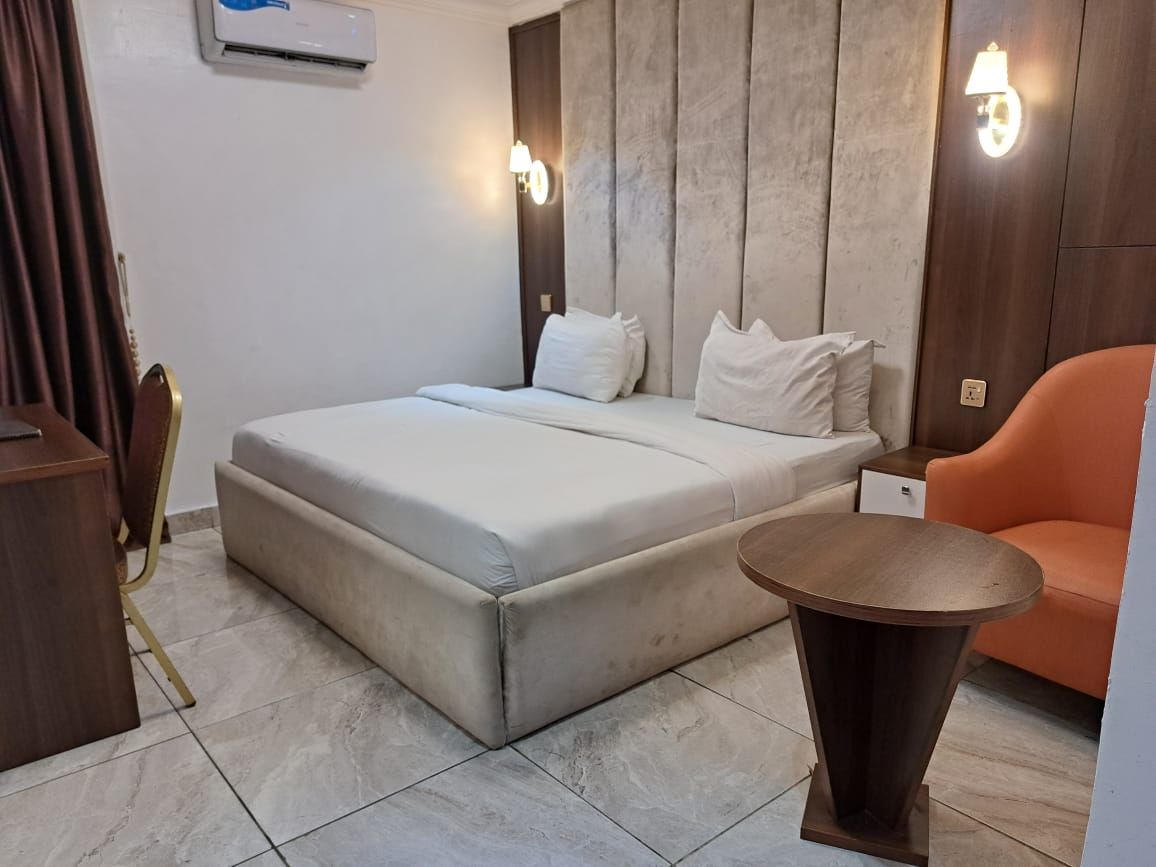 Une chambre à coucher avec un lit, une table ronde, une chaise orange et un climatiseur fixé au mur.