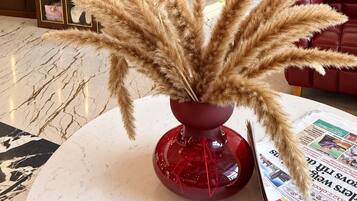 Un moderno vestíbulo de hotel con una mesa redonda de mármol, un jarrón rojo con plumas de pampa, un sofá de cuero rojo y un letrero de Budweiser.