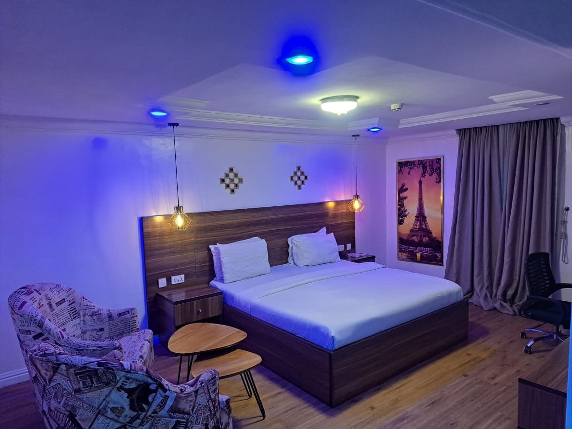 A modern hotel room with a large bed, a nightstand, a chair, a small table, and a painting of the Eiffel Tower.
