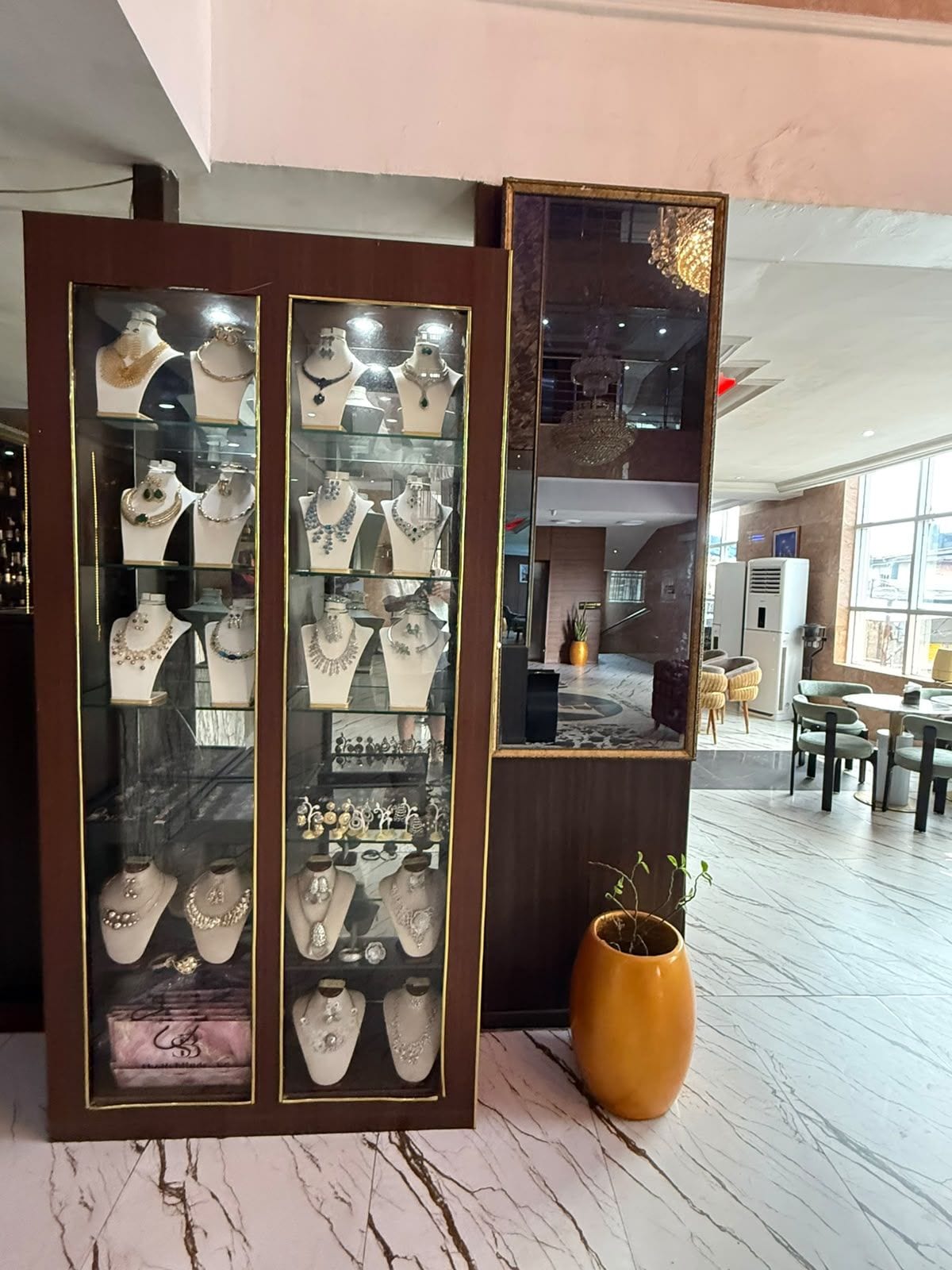 A jewelry display with multiple glass cases, a marble floor, and a yellow vase.