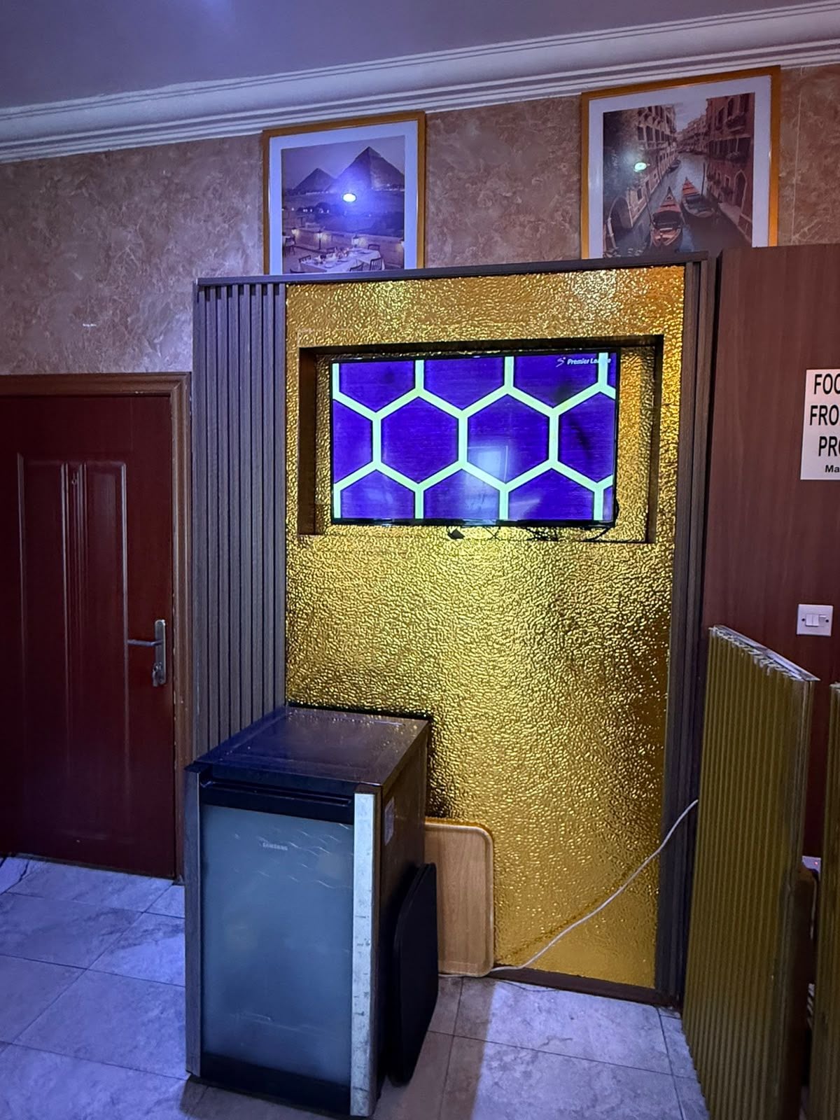 A room with a door, a small table, a radiator, and a wall with a hexagonal window.