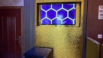 A room with a door, a small table, a radiator, and a wall with a hexagonal window.