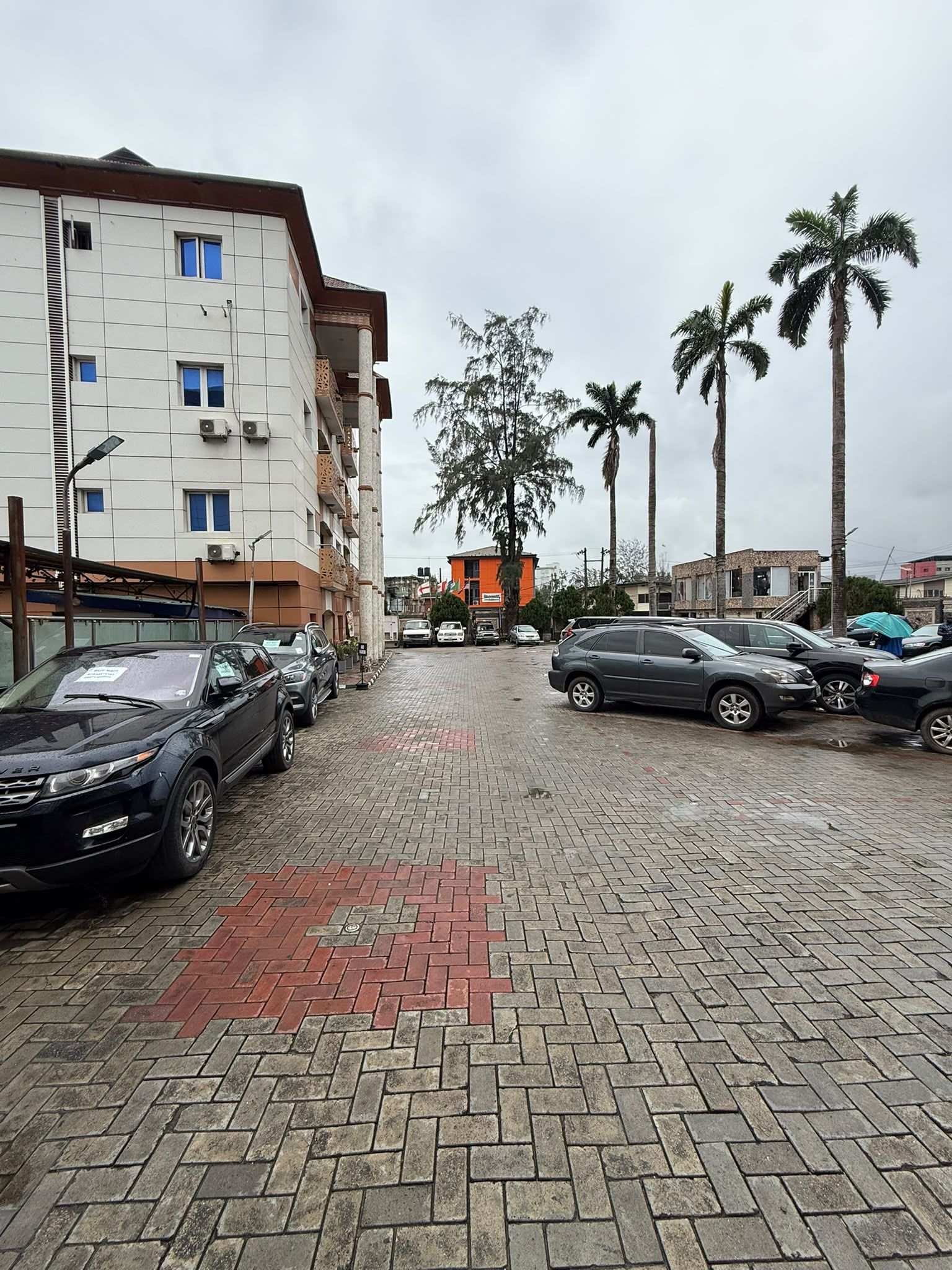 Un estacionamiento con coches, un edificio de varios pisos y palmeras.