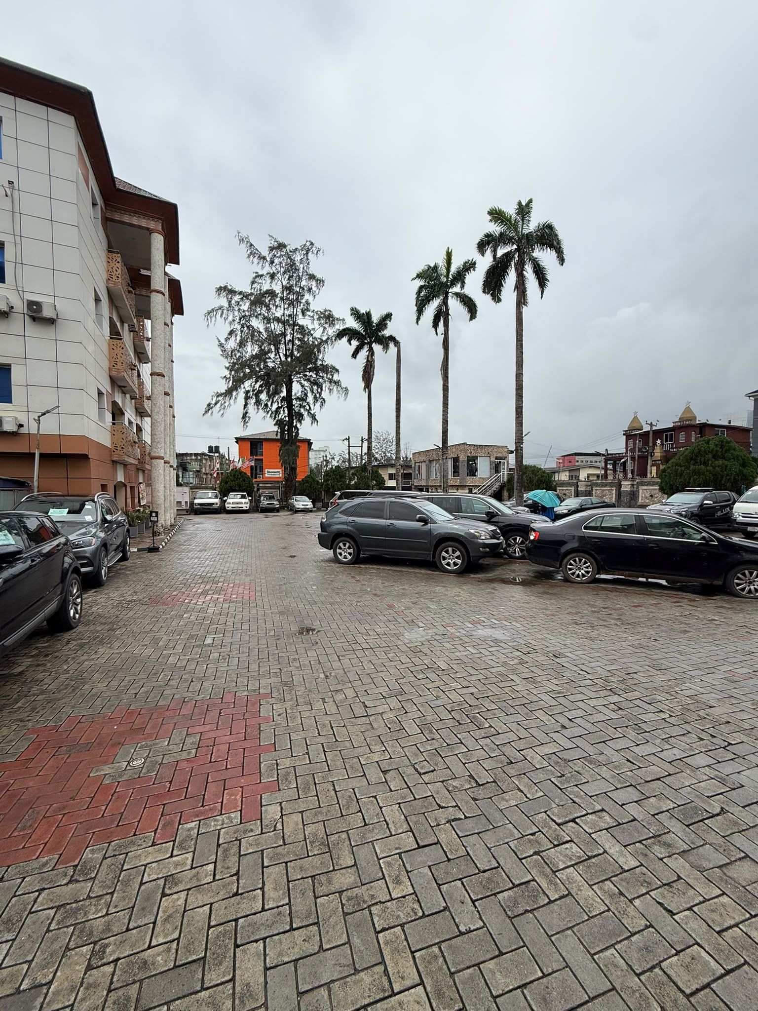 Un parking rempli de voitures, un immeuble avec des balcons et des palmiers.