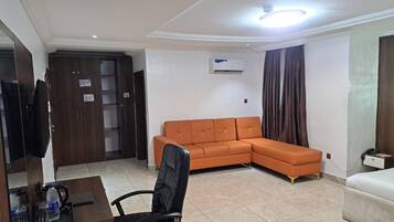 A room with a sofa, a desk with a chair, a bed, and an air conditioning unit.