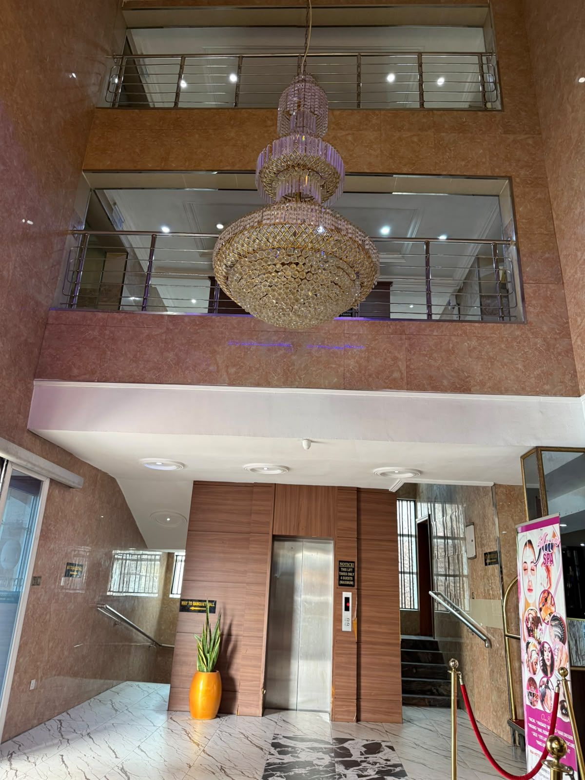 Un vestíbulo de hotel con una gran araña, un ascensor y una recepción.