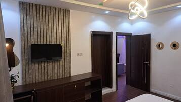 Un dormitorio moderno con una cama grande, un televisor montado en una pared de paneles de madera, un aparador de madera oscura y una puerta que da a otra habitación.