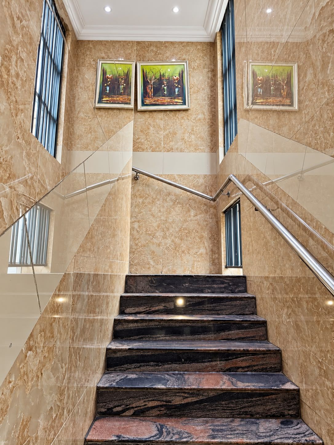 A marble staircase with handrails, leading to a landing with three framed artworks on the wall.