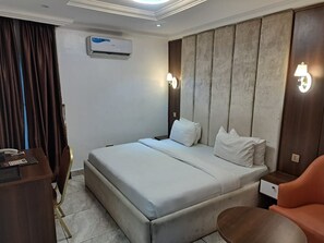 A hotel room with a bed, a desk, a chair, a bedside table, and a lamp. - R and A City Hotel  (Lagos)