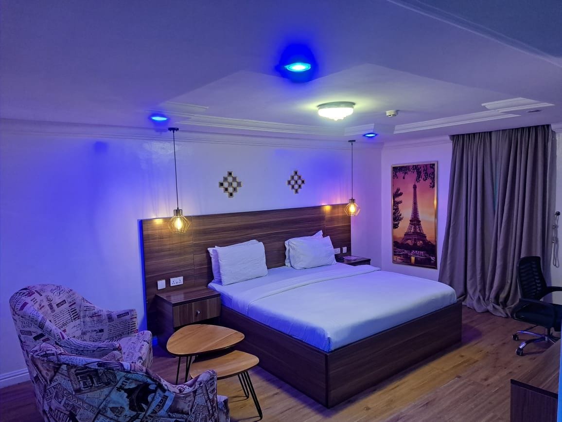 Une chambre d’hôtel avec un grand lit, une table de chevet, une chaise, une petite table ronde et un tableau accroché au mur.