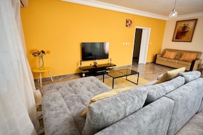 A living room with a sofa, a coffee table, a TV, and a yellow wall.
