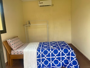 A small, single-bed room with a wooden headboard, a patterned pillow, and a blue and white bedspread.