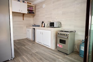 A compact kitchen with white cabinets, a microwave, an oven, and a gas cylinder.