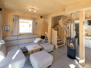 Interior acollidor d'una cabana amb un sofà, un otomà, una escala de fusta i un foc de llenya.